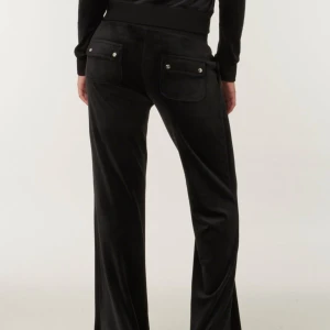 Svarta mjukisbyxor från Juicy Couture - Säljer ett par svarta mjukisbyxor från Juicy Couture i storlek XS. Byxorna har en bekväm passform med snörning i midjan och fickor med knappar bak.