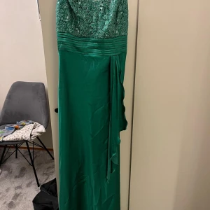 Grön axelbands långklänning - Elegant grön axelbands långklänning med spetsdetaljer på överdelen och ett vackert fall. Perfekt för festliga tillfällen.