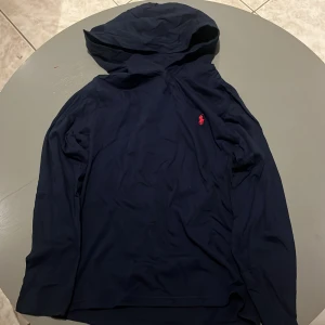 Mörkblå hoodie från Polo Ralph Lauren - Snygg mörkblå hoodie från Polo Ralph Lauren med det klassiska röda logotypen på bröstet. Perfekt för er som vill hoppa på trenden med unika ralph lauren hoodies ni i vinter. Hoodies är i storlek xs = största barn storlek. Helt oanvänd då den var för liten för mig som e 185. 10/10 kondition. Pris kan diskuteras vid snabb affär