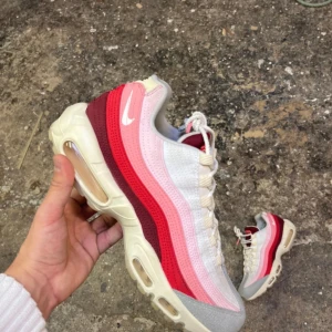 Nike sneakers i röd och vit - Snygga Nike sneakers med en vågad design i röd, rosa och vit. Skorna har en synlig luftdämpning i sulan och snörning framtill. Perfekta för en sportig look.