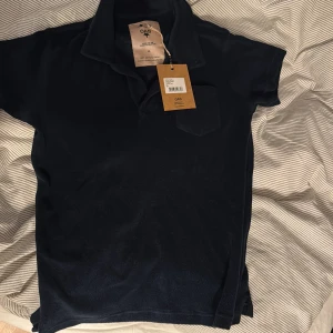 Mörkblå pikétröja från OAS - Säljer en stilren mörkblå pikétröja från OAS. Tröjan är tillverkad i mjuk frotté och har korta ärmar. Perfekt för stiligare tillfällen men även vardagen. Märkesetikett och originaltaggar kvar.