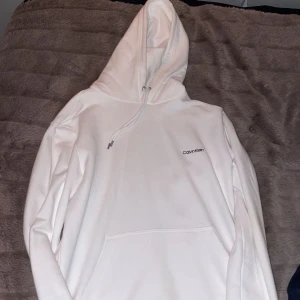 Vit hoodie från Calvin Klein - Säljer en stilren vit hoodie från Calvin Klein. Den har en klassisk design med en känguruficka och justerbar huva. Oanvänd. Storlek M.