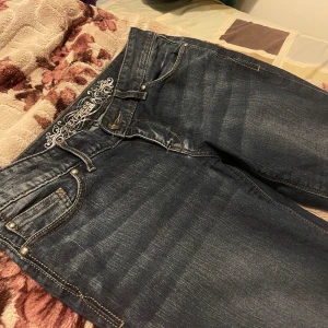 Mörkblå jeans från Express jeans  - Snygga mörkblå jeans från Express med broderade detaljer vid linningen. De har en klassisk femficksdesign och en bekväm passform. Perfekta för en avslappnad stil.