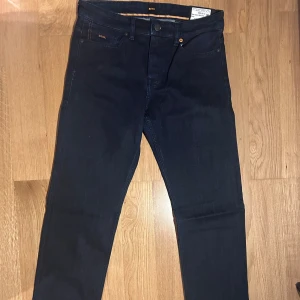 Mörkblåa jeans från Boss - Snygga mörkblå jeans från Boss i slim fit. Klassisk design med fem fickor. Perfekta för en stilren look. HELT NYA.  Modellen 'DELAWARE'. Storlek W30 L34. NYPRIS 1099