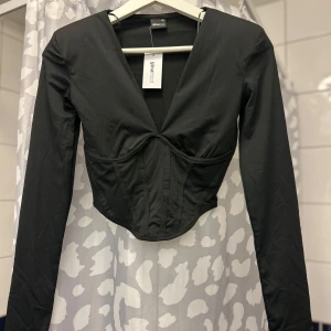 Svart långärmad topp från Gina Tricot - Snygg svart långärmad topp från Gina Tricot med en djup v-ringning och figurnära passform. Perfekt för en stilren look.