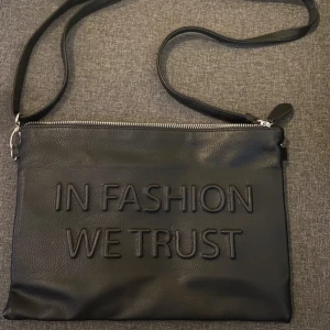 Svart axelväska med text - Aldrig använd. Axelremsväska med dragkedja samt avtagbart axelband. Finns en liten ficka inuti (bild 3). Skriv för mer info samt bilder. Katt finns i hemmet!