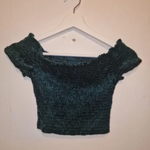 Grön offshoulder topp - Snygg grön offshoulder. Toppen är croppad och har en smockad design som ger en tight passform. Garderobsrensning så kika gärna på övriga auktioner.