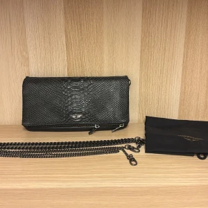 Svart kuvertväska från Zadig & Voltaire - Jag säljer min super fina Zadig & Voltaire väska, då den inte kommer till användning längre. Snygg svart kuvertväska i skinn från Zadig & Voltaire med ormskinnsmönster. Väskan har en kedja som axelrem och en praktisk dragkedja på baksidan. Original priset för väskan är 4000kr men jag säljer den nu för 1250 priset går att diskuteras!❤️