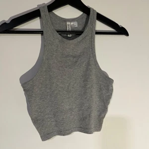 Grå ribbad linnetopp från H&M - Snygg grå ribbad linnetopp. Perfekt för en casual look med sin croppade design och ärmlösa stil. Passar bra till både jeans och kjol.