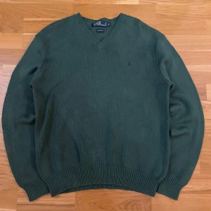 Grön stickad tröja från Polo Ralph Lauren - Säljer en stilren grön stickad tröja från Polo Ralph Lauren i 100% bomull. Tröjan har en v-ringad hals och ett diskret broderat logotypmärke på bröstet. Perfekt för en avslappnad och klassisk look.