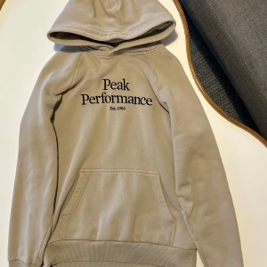 Beige hoodie  Peak Performance. - Säljer en snygg beige hoodie från Peak Performance med svart text på bröstet. Riktigt bra kvalitet. Snören saknas men inget man märker.