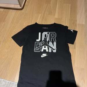 Svart t-shirt från Jordan - Snygg svart t-shirt från Jordan med det ikoniska Jumpman-logotypen på bröstet och ärmen. Perfekt för sportiga tillfällen eller en avslappnad stil. Tillverkad i mjukt material för komfort.