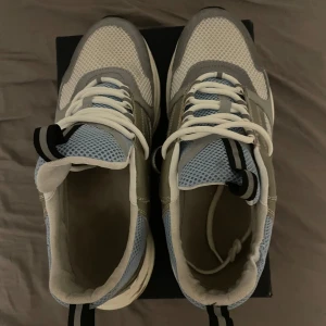 Grå och blå sneakers med snörning - Snygga sneakers i grått och blått med vit sula och snörning. Skorna har ett sportigt utseende med meshdetaljer för extra andningsförmåga. Perfekta för en casual look.
