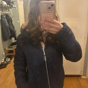 Mörkblå Gant pufferjacka med dragkedja - Säljer en snygg mörkblå gant pufferjacka med dragkedja. Jackan har en mysig huva och långa ärmar, perfekt för kyliga dagar. Den quiltade designen ger extra värme och stil.