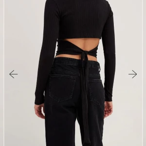 Svart ribbad topp med knytning - helt ny - Trendig svart ribbad topp med långärmad design och knytning i ryggen. Perfekt för en stilren look. Från NAKD
