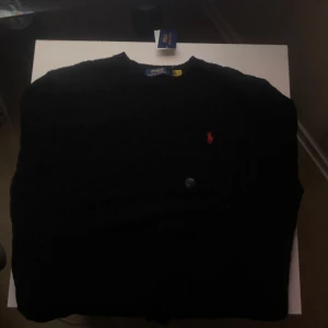 Svart stickad tröja från Polo Ralph Lauren - Snygg svart stickad tröja från Polo Ralph Lauren med klassiskt kabelstickat mönster. Perfekt för en stilren look. Storlek: M Helt ny tröja aldrig använt (Kvitto finns!)
