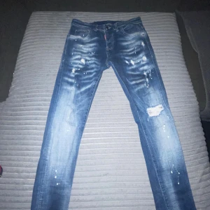 DSQUARED2 JEANS - Snygga blå jeans från Dsquared2 med slitna detaljer och en cool tvättad look. De har en knappgylf och klassisk femficksdesign. Perfekta för en avslappnad stil.