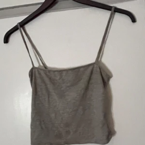 Grå linnetopp från Divided - Säljer en enkel och stilren grå linnetopp från Divided. Toppen har smala axelband och är perfekt för varma dagar. Passar bra till både jeans och kjol.