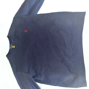 Mörkblå tröja från Polo Ralph Lauren - Säljer en stilren mörkblå tröja från Polo Ralph Lauren med det klassiska röda logotypbroderiet på bröstet. Tröjan har långa ärmar och en rund halsringning. Perfekt för en avslappnad och snygg look.
