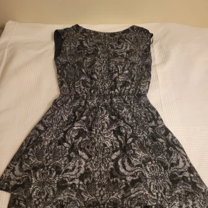 Svart och vit mönstrad klänning från H&M - Snygg svart och vit klänning från H&M med ett intrikat mönster. Klänningen är ärmlös och har en normal passform. Tillverkad i 100% polyester, vilket gör den lätt och bekväm att bära.