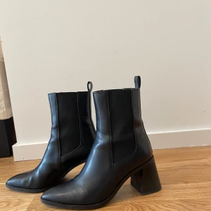 Svarta boots med klack - Snygga svarta boots i skinn med klack och spetsig tå. Perfekta för en stilren look, dessa boots har en klassisk design med dragflikar upptill för enkel påtagning.
