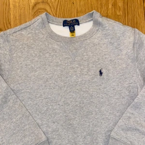 Grå tröja från Polo Ralph Lauren - Säljer en stilren grå tröja från Polo Ralph Lauren med det klassiska logotypbroderiet på bröstet. Tröjan har rund hals och långa ärmar, perfekt för en avslappnad look. Tveka inte om ni har frågor! Om ni köper något mer från min profil så får ni alltid paketpris. Tröjan säger M 10-12 jag skulle säga att den passar någon som är 11 ungefär!