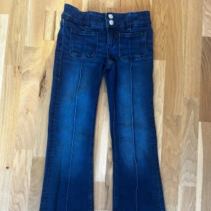 Mörkblå jeans från Gina Tricot - Snygga mörkblå jeans från Gina Tricot med två knappar i midjan och framfickor. Perfekta för en stilren look med en bootcut-stil som ger en trendig touch.