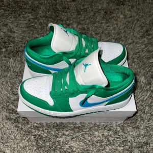Nike Air Jordans  - Snygga Nike Air Jordans i en fräsch grön och vit färgkombination. Skorna har en klassisk design med snörning och en blå detalj på sidan. Perfekta för dig som vill ha en stilren look med en färgklick.