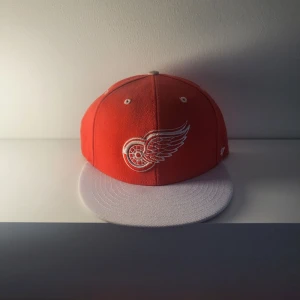 Röd keps med broderad logotyp - Snygg snapbacks  röd keps med broderad logotyp på framsidan och texten 'Red Wings' under skärmen. Perfekt för sportfantasten!