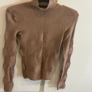 Brun ribbad polotröja från Lamise - Snygg brun polotröja från Amisu med ett unikt ribbat mönster. Tröjan har långa ärmar och en hög krage som ger en stilren look. Perfekt för kyligare dagar.Aldrig använd!