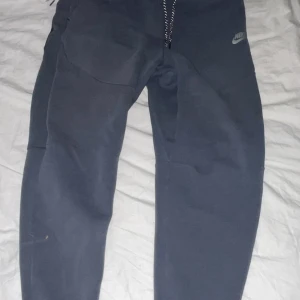 Mörkblå mjukisbyxor från Nike - Säljer ett par mörkblå mjukisbyxor från Nike i storlek S. Byxorna har en bekväm passform med snörning i midjan och en praktisk ficka på sidan. Perfekta för en avslappnad stil eller träning.