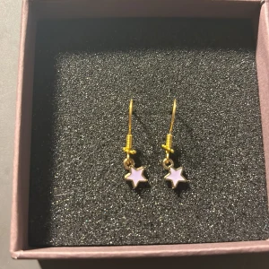 Guldörhängen med stjärnor - Säljer ett par superfina guldörhängen med små stjärnor som hänger ner. Stjärnorna har en vit mitt och är perfekta för att ge en extra touch till din outfit. Passar både till vardag och fest!