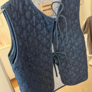Blå quiltad väst från Damson Madder - Säljer en superfin blå quiltad väst från Damson Madder. Den har en snygg knytning framtill och är perfekt för lager-på-lager-stilen. Västen är i storlek 10 och har en cool, mönstrad insida. Perfekt för höst och vår! Nypris: 900kr