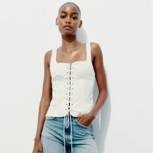 Vit ribbad korsett-topp - Snygg vit ribbad korsett-topp med snörning framtill. Toppen är ärmlös och har en tight passform som framhäver figuren. Perfekt för sommarens alla fester! Använt 1 gång och enda ”defekten” är att jag vikte den lite i slutet så behöver strykas.💕