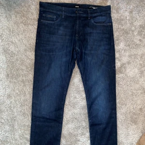 Mörkblå jeans från Hugo Boss - Säljer ett par mörkblå jeans från Hugo Boss. De är i slim fit och tillverkade av lättviktsdenim. Jeansen har en klassisk femficksdesign och en läderpatch med BOSS-loggan på baksidan. De är i bra skick 