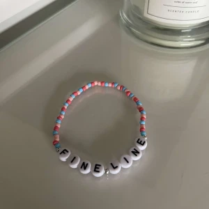 Färgglatt pärlarmband med text - Säljer ett supergulligt armband med färgglada pärlor i rosa, blått och vitt. Armbandet har bokstavspärlor som bildar texten 'FINE LINE'. Perfekt för att ge en personlig touch till din outfit!