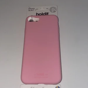 Rosa mobilskal från Holdit - Säljer ett snyggt rosa mobilskal från Holdit, designat för iPhone SE/8/7. Skalet är en del av The Essential Collection och stödjer trådlös laddning. Perfekt för att skydda din telefon med stil!