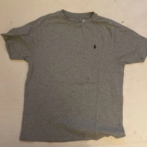 Grå t-shirt från Polo Ralph Lauren - Säljer en klassisk grå t-shirt från Polo Ralph Lauren med en liten broderad logga på bröstet. T-shirten är kortärmad och tillverkad i mjuk bomull, perfekt för en avslappnad stil.
