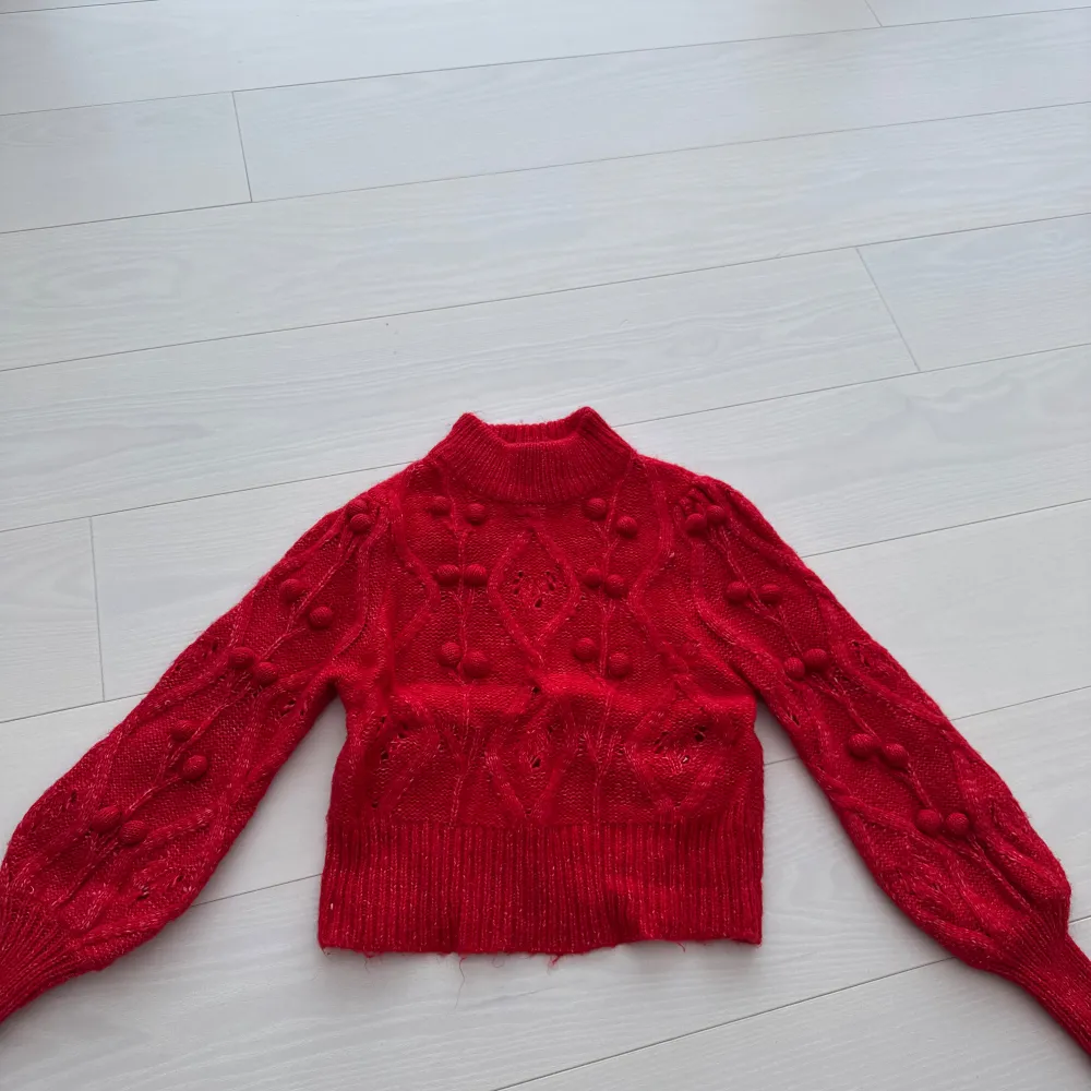 Säljer en snygg röd stickad tröja med unikt mönster och puffiga detaljer. Tröjan är croppad och har långa ärmar, perfekt för kyligare dagar. Passar bra till både jeans och kjol. Ett måste i garderoben för den stilmedvetna!. Neuletakit & Villapaidat.