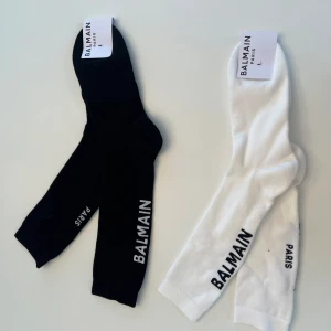 Svarta och vita strumpor från Balmain - Snygga strumpor från Balmain i svart och vitt med texten 'BALMAIN PARIS' längs sidan. Perfekta för att ge en lyxig touch till din outfit. Tillverkade i Italien. Helt nya