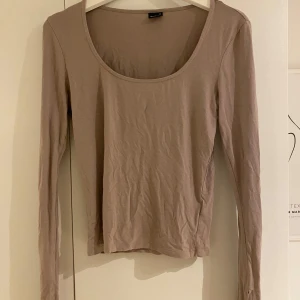 Beige långärmad topp från Gina Tricot - Säljer en stilren beige långärmad topp från Gina Tricot. Toppen har en rundad halsringning och är tillverkad i ett mjukt material som ger en bekväm passform. Perfekt för lager-på-lager eller som den är. Slits på handleden