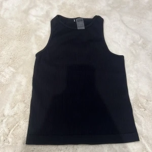 Svart ribbad linnetopp från Stronger - Snygg svart ribbad linnetopp från Stronger. Perfekt för en stilren look. Tillverkad i polyester och elastan för en bekväm passform.