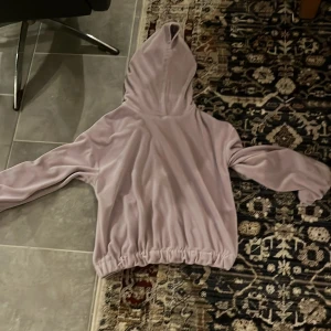 Ljuslila hoodie med text - Säljer en mysig ljuslila hoodie med texten 'New Day' på ärmen. Tröjan har en luva och långa ärmar, perfekt för en avslappnad stil. Den elastiska nederkanten ger en bekväm passform.