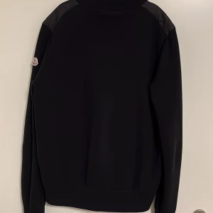 Moncler Cardigan - Den populära cardiganen från Moncler! Den är en del använd och en lapp har tyvärr lossnat halvt (bild 4). Men utöver det är den i fint skick, skulle säga 8/10 skick