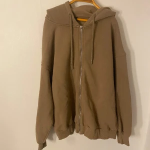 Beige hoodie med dragkedja - Säljer en beige hoodie med dragkedja och huva. Tröjan har långa ärmar och ribbade muddar vid ärmslut och nederkant. Perfekt för en avslappnad stil.