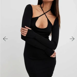 Svart klänning med knytning runt halsen  - Svart kort klänning med långärmad design och knytning i halsen. Banden kan knytas runt halsen som de är eller korsas över bröstet för en extra detalj. 