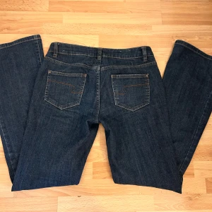 Blå low waist bootcut jeans - Snygga blå jeans med klassisk femficksdesign och knappgylf. Perfekta för en avslappnad stil med en bootcut passform.