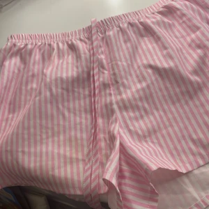 Randiga shorts med knytband - Säljer två par randiga shorts i bomull, ett par i rosa och vitt och ett par i blått och vitt. Båda har elastisk midja och knytband för justerbar passform. Perfekta för en avslappnad stil.