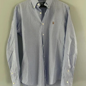 Rutig skjorta från Polo Ralph Lauren - Snygg rutig skjorta från Polo Ralph Lauren i blått och vitt. Skjortan har långa ärmar och klassiska knappar framtill. Perfekt för en stilren look med en liten broderad logga på bröstet. Perfekt för midsommar eller vilket firande som helst 🍾🦸‍♂️✅😉🥂
