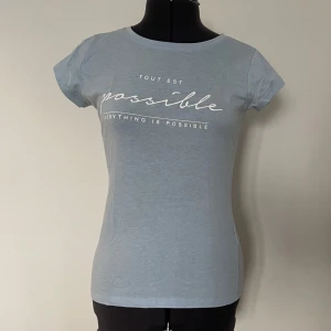 Ljusblå t-shirt med text - Ljusblå t-shirt med texten 'Tout est possible, everything is possible' tryckt på framsidan.